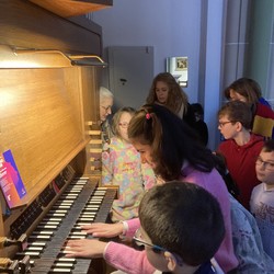 Foto von Vida beim Spielen auf der Orgel,  die Gruppe sieht zu (vergrößerte Bildansicht wird geöffnet)