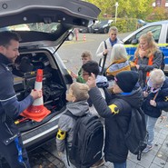 Foto der Gruppe am Kofferraum des Polizeiautos mit Pylon (vergrößerte Bildansicht wird geöffnet)