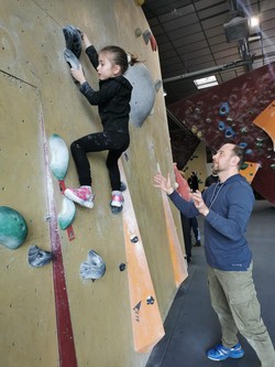 Foto von Hafsa an der Boulderwand. Herr Nagel steht auf dem Boden und unterstützt sie (vergrößerte Bildansicht wird geöffnet)