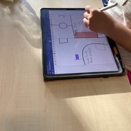 Eine Schülerin sitzt vor ihrem iPad, auf dem sie mit ihrem Apple Pencil ein Haus farbig ausmalt. (vergrößerte Bildansicht wird geöffnet)