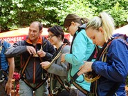 Foto von Schülern bei der Ankleidung mit Gurten und Einweisung zum Klettern (vergrößerte Bildansicht wird geöffnet)