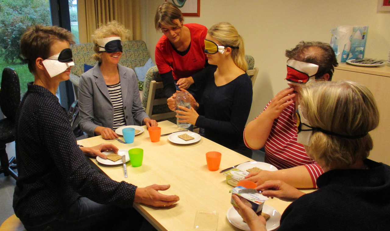 Menschen mit verbundenen Augen sitzen um einen gedeckten Tisch