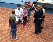 Foto von Sven Buick beim Binden des Karate-Gürtels bei einer Schülerin (vergrößerte Bildansicht wird geöffnet)