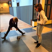 Foto von zwei Schülerinnen, die ihrem Roboter auf dem Boden fahren lassen (vergrößerte Bildansicht wird geöffnet)