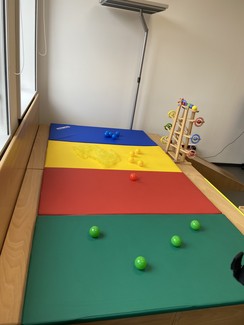 Auf dem Bild ist eine Turnmatte in grün, rot, gelb und blau zu sehen, auf der kleine Bälle liegen