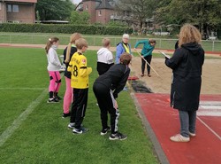 Foto von Schüler:innen und Lehrer:innen an der Weitsprunganlage (vergrößerte Bildansicht wird geöffnet)