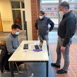 Foto von Tim an seinem Tisch zu seinen Praktika mit Besuchern (vergrößerte Bildansicht wird geöffnet)