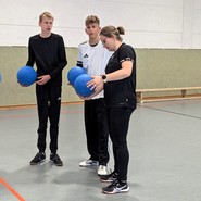 Annkathrin steht neben Mattis und Tom und alle halten einen Goalball in der Hand. (vergrößerte Bildansicht wird geöffnet)