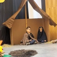 Foto: Die Kinder in ihren Rollen von Maria und Josef sitzen geduldig im Stall und warten auf ihren Einsatz (vergrößerte Bildansicht wird geöffnet)