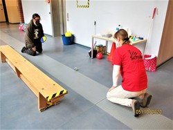 Foto von einer Teilnehmerin mit Kursleiterin beim Zurollen eines Balls mit Simulationsbrille (vergrößerte Bildansicht wird geöffnet)