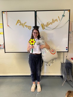 Foto von Kira Materna mit Blume und Luftballon-Einhorn vor einer Tafel mit der Aufschrift "Prüfung bestanden"