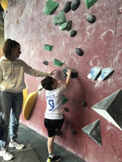 Foto von Havan an der Boulderwand. Er erhält eine Einweisung durch Mitarbeiterin. (vergrößerte Bildansicht wird geöffnet)