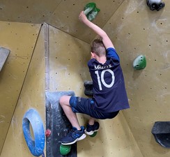 Foto: Ein Schüler klettert an einer Wand. Er steht auf zwei Griffen und hält sich ebenso mit beiden Händen fest.