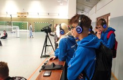 Mattis steht hinter einer Bande und hat Kopfhörer auf über die er das Spiel per Audiodeskription verfolgt