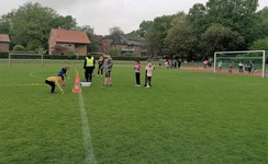 Foto von Sportler:innen und Betreuer:innen auf dem Sportplatz bei Wolkenhimmel