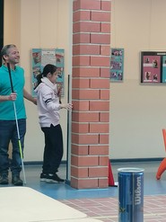 Eine ältere Schülerin steht frontal zu einer Säule in der Aula, Juan Ruiz hält sie am Ellenbogen. Er selbst hält in der anderen Hand einen Langstock. (vergrößerte Bildansicht wird geöffnet)