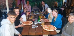 Das Team sitzt abends zusammen draußen in einem Restaurant und isst Burger oder Pizza.