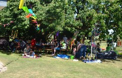 Foto der Teilnehmer unter einem großen Baum mit Tischen, Bänken Picknick-Decken und Dekoration